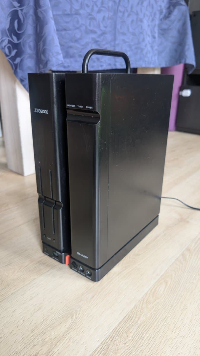 Sharp X68000 computer in black vertical case with handle, reassembled after extensive repair work including recapping and FDD surgery, positioned on wooden surface.