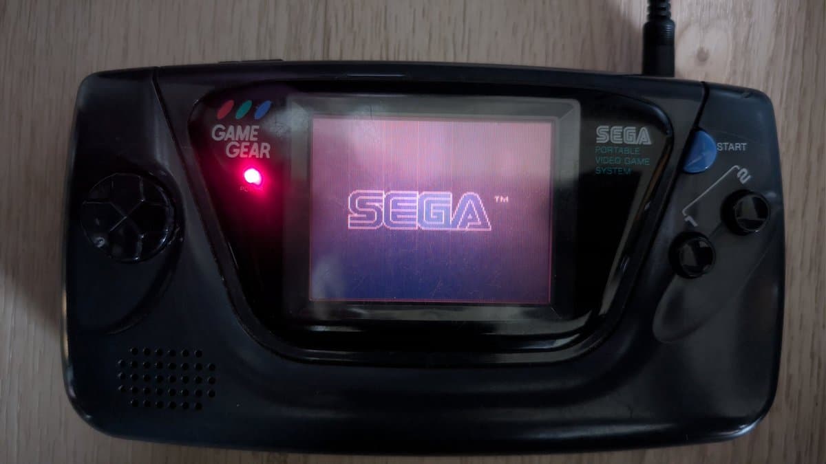 Sega Game Gear displaying startup screen with red power LED lit; screen now functional after repair work, console still experiencing random power-off issues.
