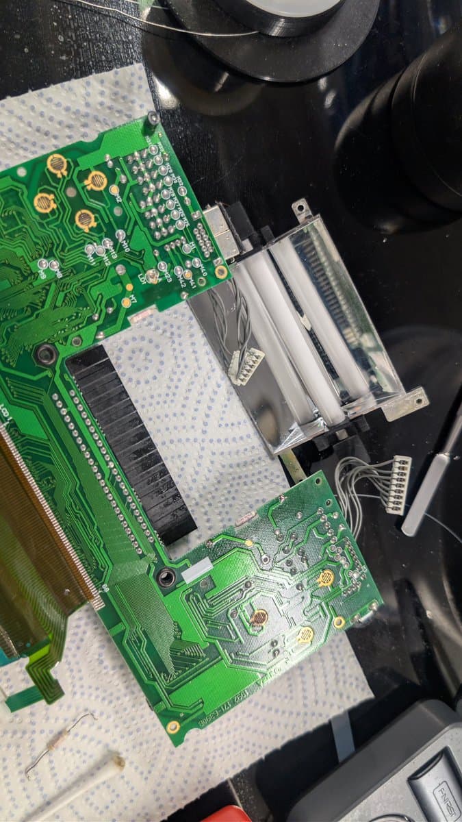 Game Gear PCB with replaced fuse; green circuit boards on white work mat with tweezers and black device above.