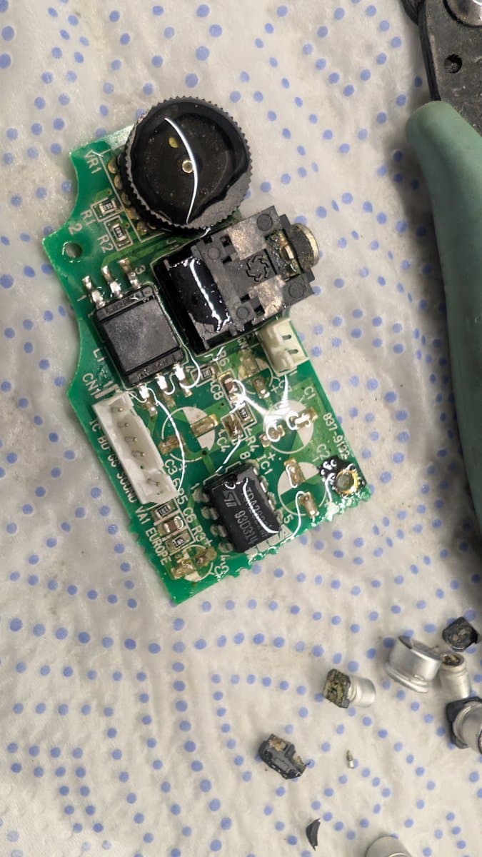 Disassembled Game Gear power board showing lifted capacitors and power jack area; vinegar-cleaned PCB with visible solder joint repairs.