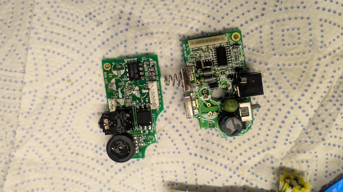 Two Sega Game Gear circuit boards on dotted surface after ultrasonic cleaning; left board shows power circuit with black connector, right board displays audio components and capacitors.