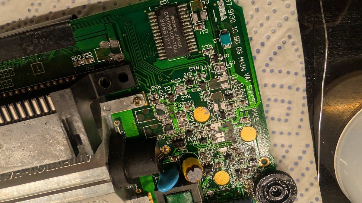 Sega Game Gear main board after cleaning, showing electrolytic capacitor damage on button pad contacts, with deoxidized components ready for capacitor replacement.