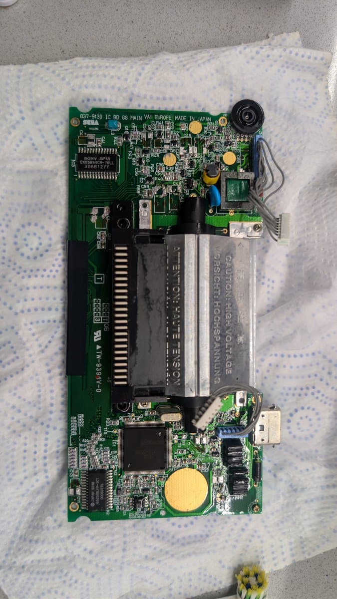 Sega Game Gear main PCB cleaned and laid out for capacitor replacement, showing corroded button pad contacts treated with Deoxit.