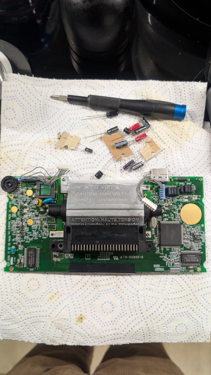 Sega Game Gear mainboard with replaced capacitors on breadboards, soldering iron, and discrete components during capacitor replacement repair work.
