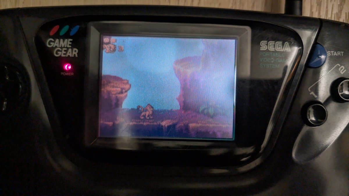 Sega Game Gear displaying The Lion King after repair work; power LED lit, screen showing gameplay after resoldering and component cleaning.