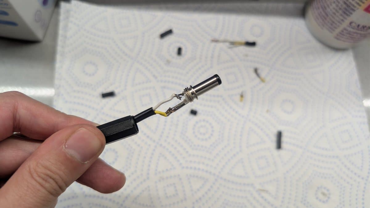 Hand holding Game Gear power connector with exposed barrel connector pins and internal wiring during external PSU restoration.