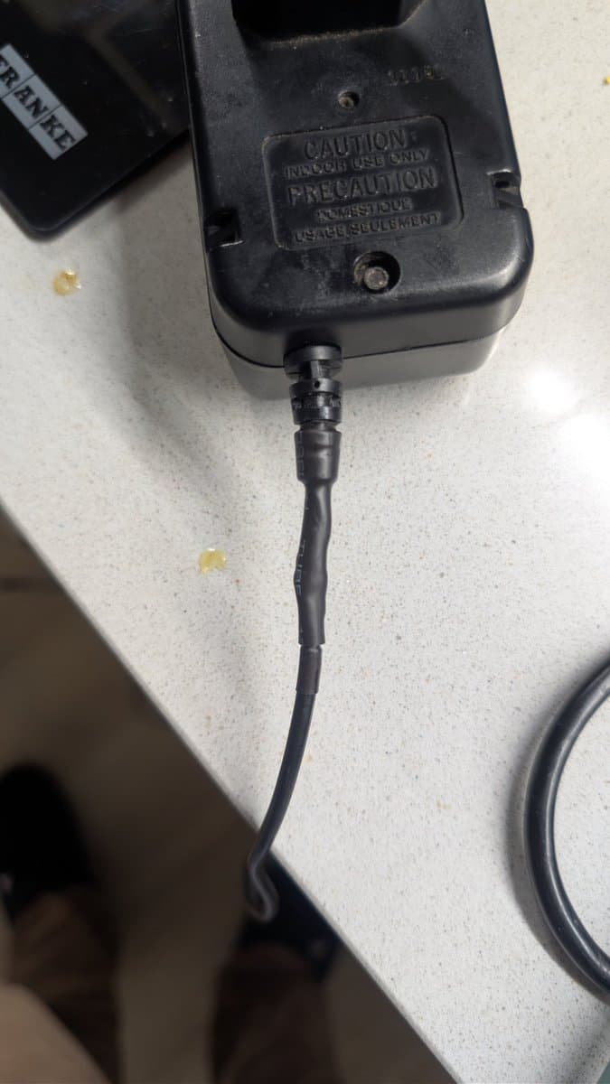 Black power adapter with "CAUTION" warning label and coiled cable on light surface during Game Gear repair.