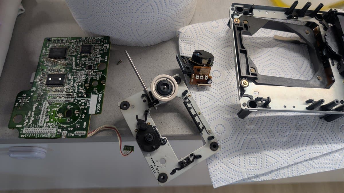 Disassembled Mega-CD 1 showing green mainboard, KSS-240A optical pickup, motor assembly, and metal chassis components laid out on work surface.