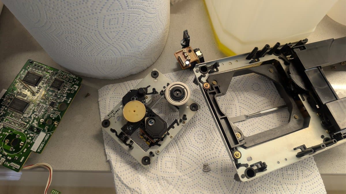 Disassembled Mega-CD 1 optical drive showing new laser pickup installed, circuit board, and mechanical housing components on work surface.