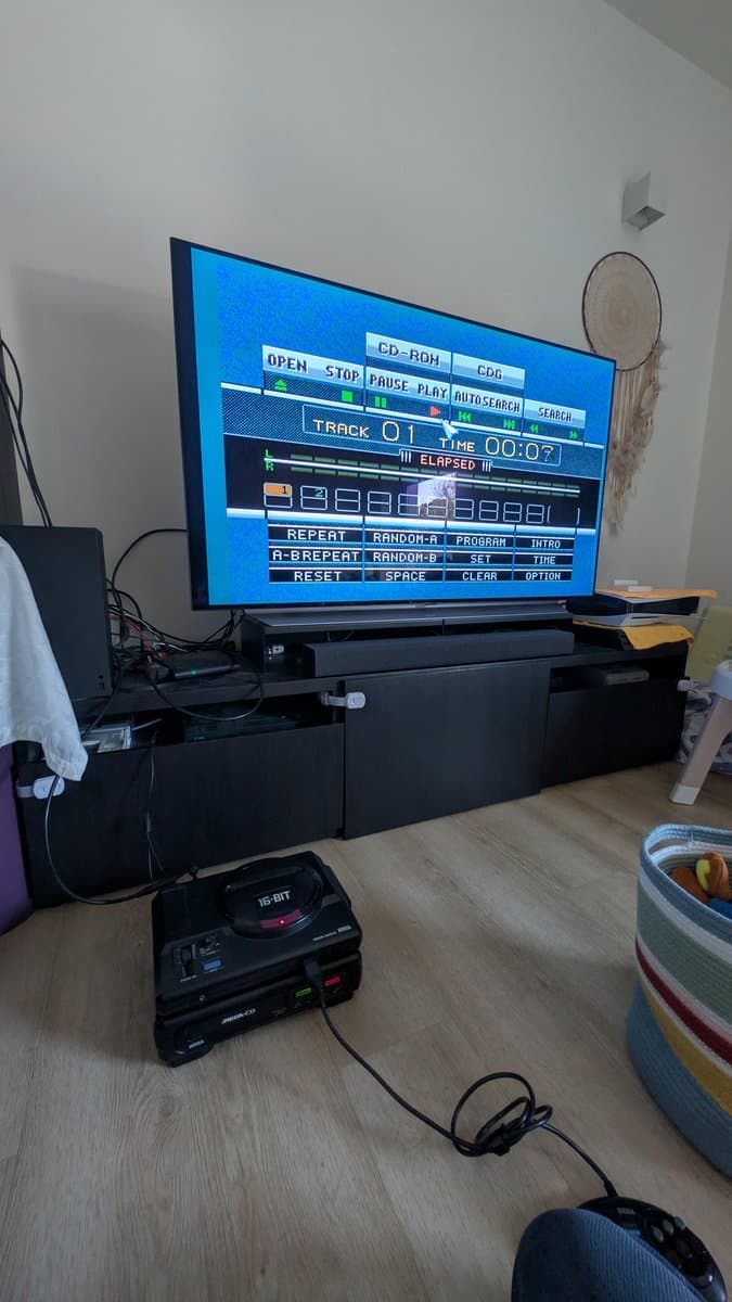 Sega Mega-CD 1 displaying CD player interface on TV screen, showing Track 01 playing with elapsed time 00:07, connected to 16-bit console below.