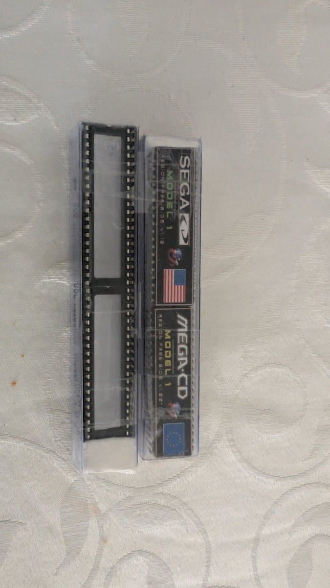 Sega Mega-CD Model 1 unit in clear plastic case showing internal circuit board with dual rows of pin connectors, displayed on textured surface.