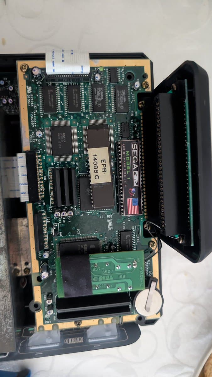 Sega Mega-CD 1 mainboard with SEGACD and ERR 4088C chips visible, yellow daughterboard attached, undergoing region unlock modification.