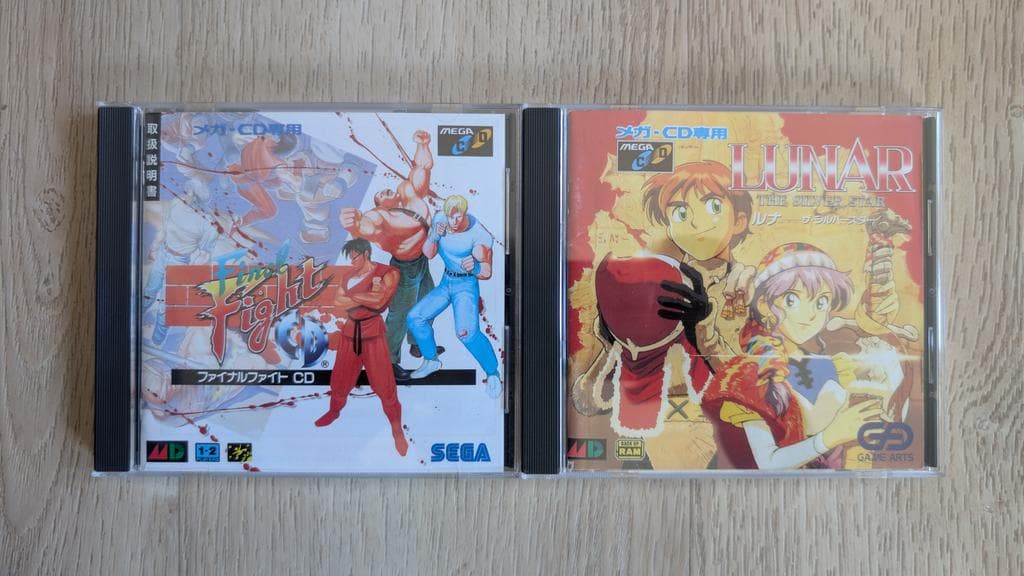 Two Sega Mega-CD game cases on wooden surface: Final Fight and Lunar, both marked for Mega-CD use, ready for restoration work.
