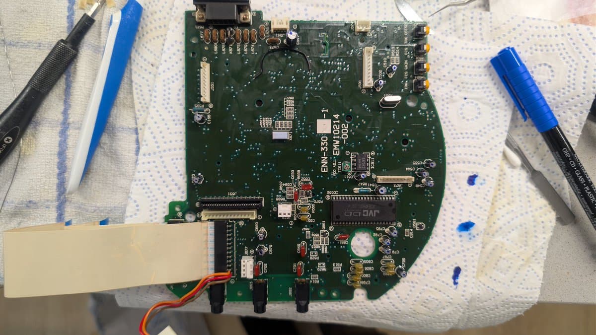 Sega Wondermega HWM-5010 CD-ROM board undergoing recapping repair, with soldering iron and tools visible on workbench.