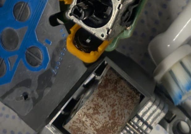 Disassembled PS4 controller showing potentiometer wiper compartment being cleaned with yellow brush tool during drift repair.