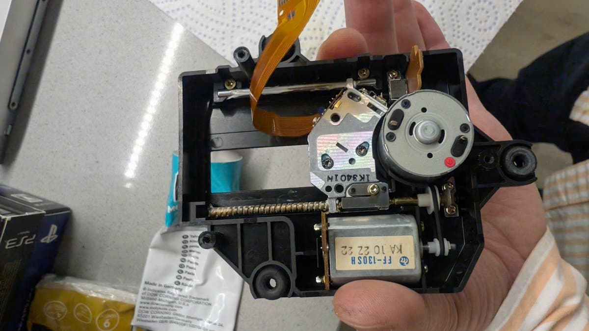 Disassembled FM Towns Marty CD-ROM drive PCB held in hand, showing motor, flex cable, laser lens assembly, and motor control components during recapping.