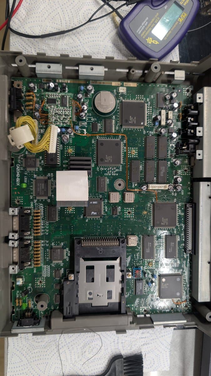 Fujitsu FM Towns Marty main board recapped; visible capacitors replaced, corrosion cleaned with vinegar/isopropyl. Multimeter nearby for testing.