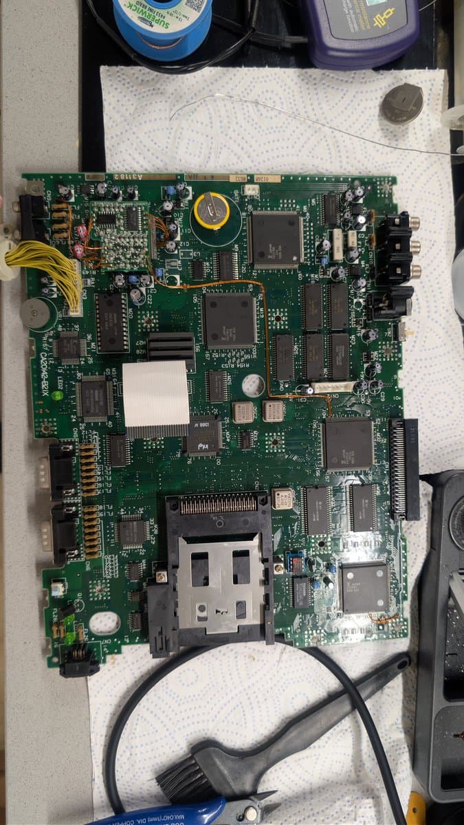 FM Towns Marty main board mid-recap: electrolytic capacitors replaced, old leaked capacitor residue cleaned, coin for scale, yellow power connector visible.