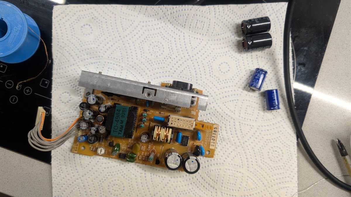 Fujitsu FM Towns Marty PSU board with newly installed capacitors; replacement black capacitors and blue capacitors displayed separately on work mat.