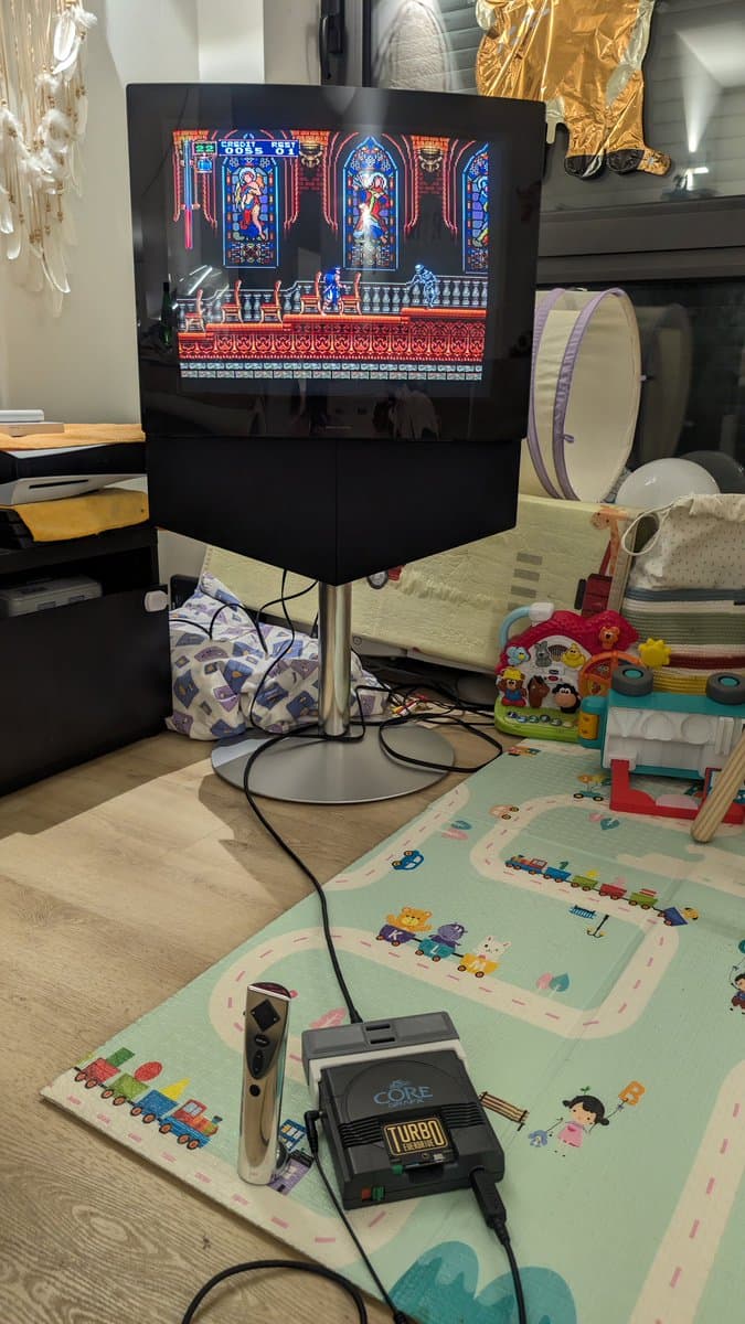 NEC PC Engine CoreGrafx displaying Rondo of Blood on monitor during recap repair testing with controllers and turbo pad on play mat.