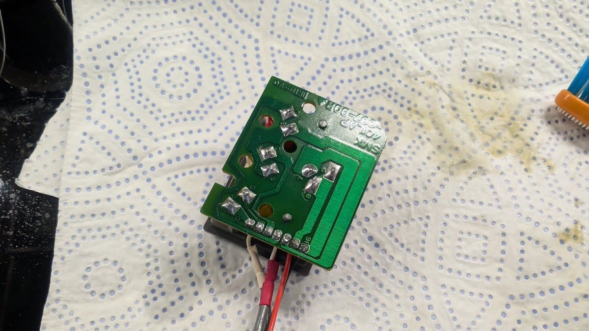 Green circuit board with replaced capacitors, voltage regulator, and supercapacitor; red wires attached; mounted on dotted work mat.