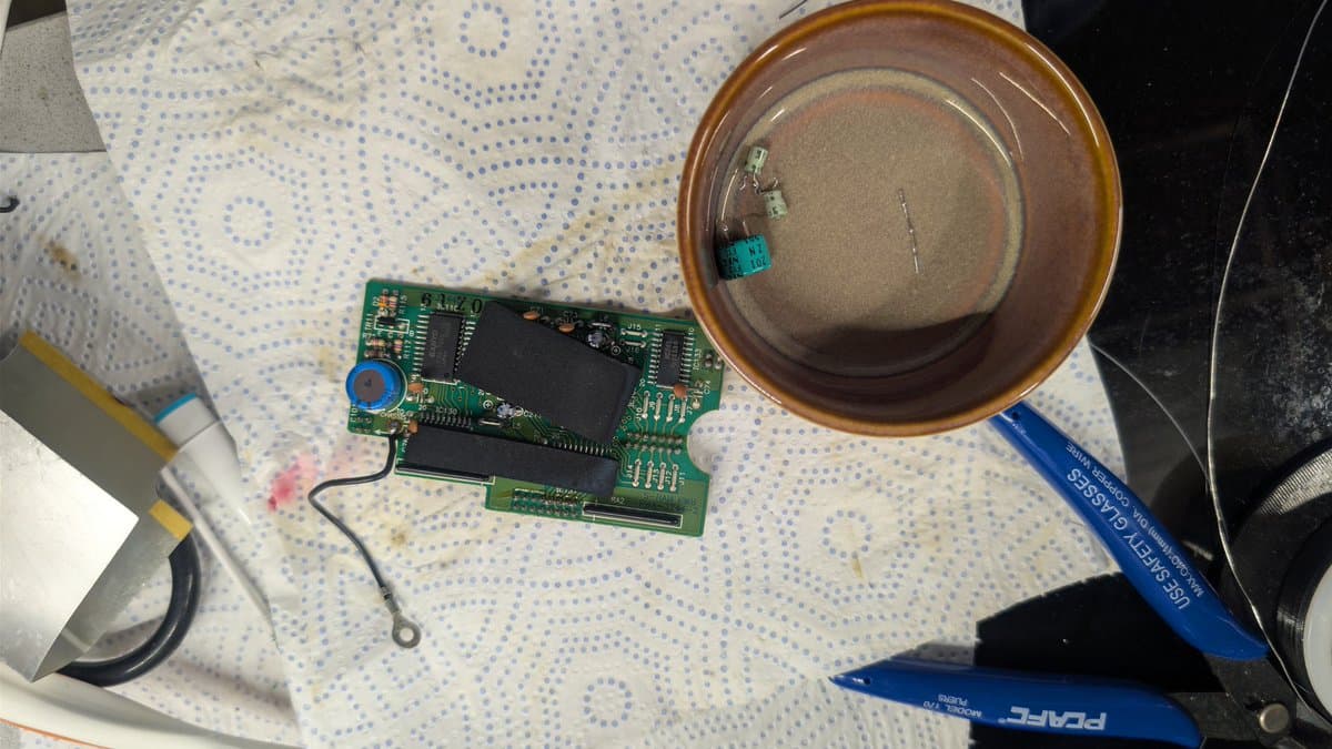 Disassembled PC Engine IFU-30 board with replaced capacitors, voltage regulator, and supercapacitor alongside desoldering tools on work surface.