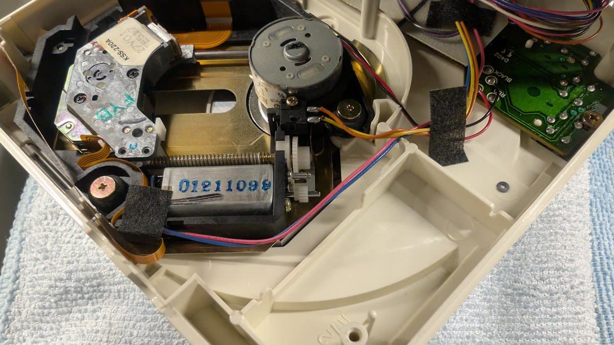 PC Engine CD-ROM2 internal mechanism showing laser assembly, motor, PCB, and wiring during restoration work on white plastic chassis.