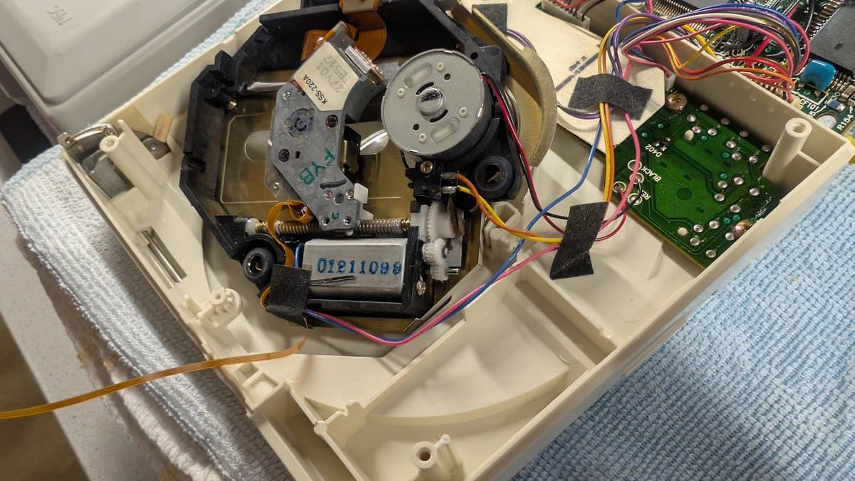 PC Engine CD-ROM2 interior showing motor, laser diode, green control board, and colored wiring during restoration work.