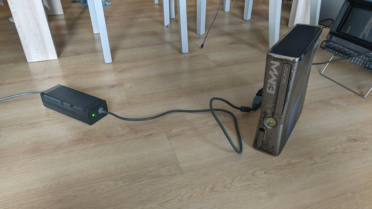 Xbox 360 S connected to external power supply via cable during post-repair testing on wooden floor.