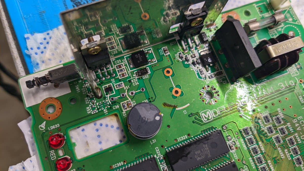 Panasonic FZ-1 motherboard mid-recap; through-hole solder joints with oxidation, capacitors, and IC chips visible during restoration work.