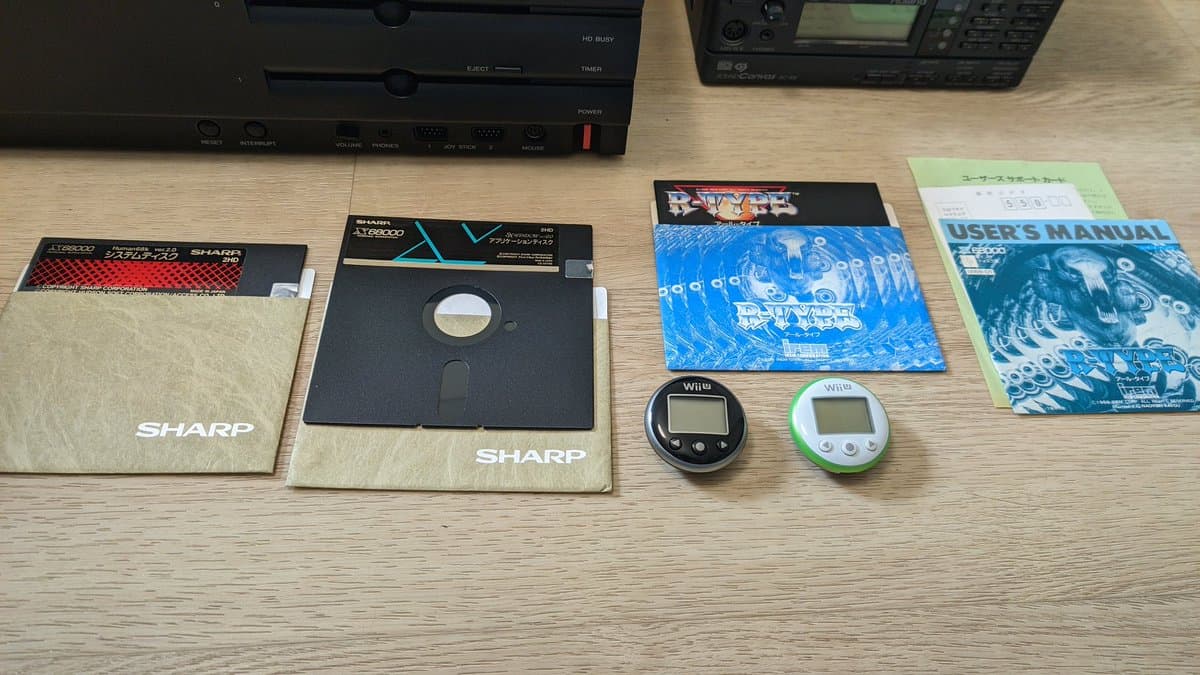 Sharp X68000 Pro II with floppy disks, game software, Wii controllers, and Roland MIDI modules on wooden desk.