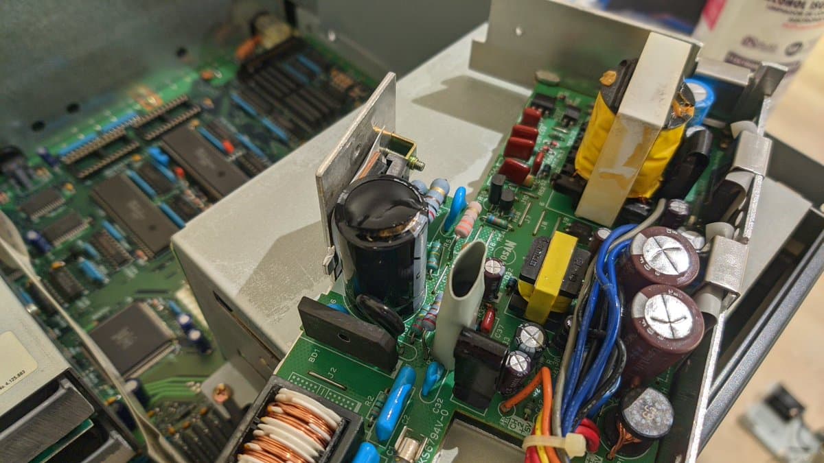 Sharp X68000 Pro II power supply board with reversed electrolytic capacitor, inductor coils, transformers, and capacitors showing damage from reverse polarity installation.