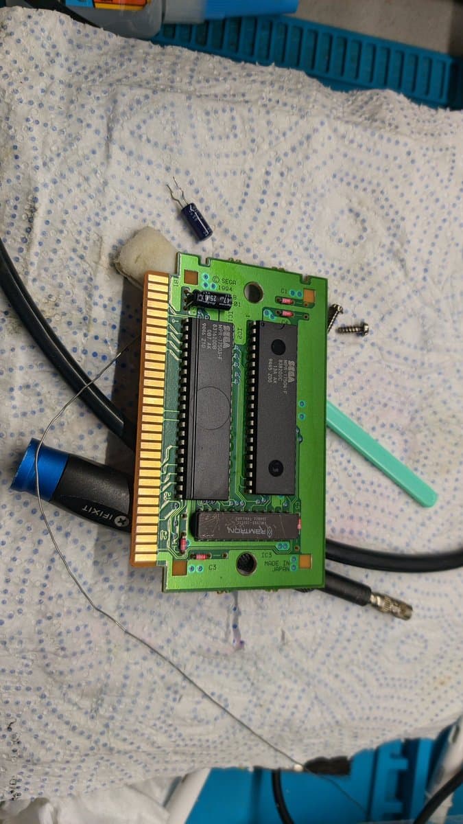 Sega 32X Virtua Racing Deluxe PCB with replaced capacitor, IPA cleaning residue, and green plastic tool on workbench.