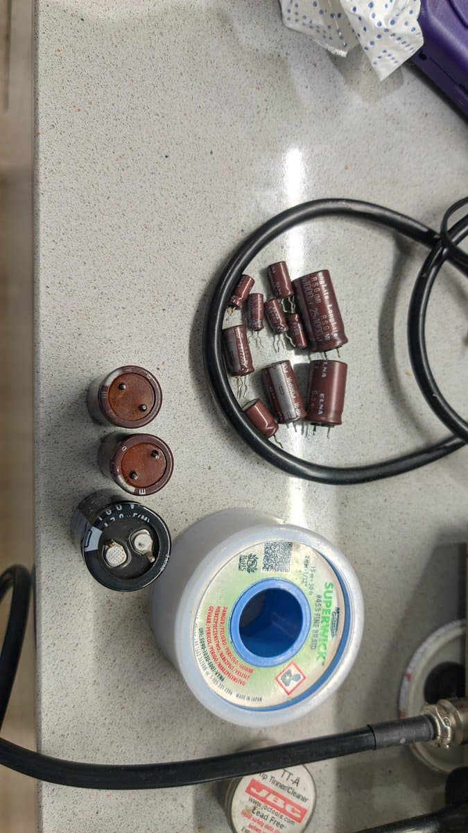 Electrolytic capacitors, solder spool, rotary switch, and reversed filter on concrete workbench during X68000 Pro II restoration.