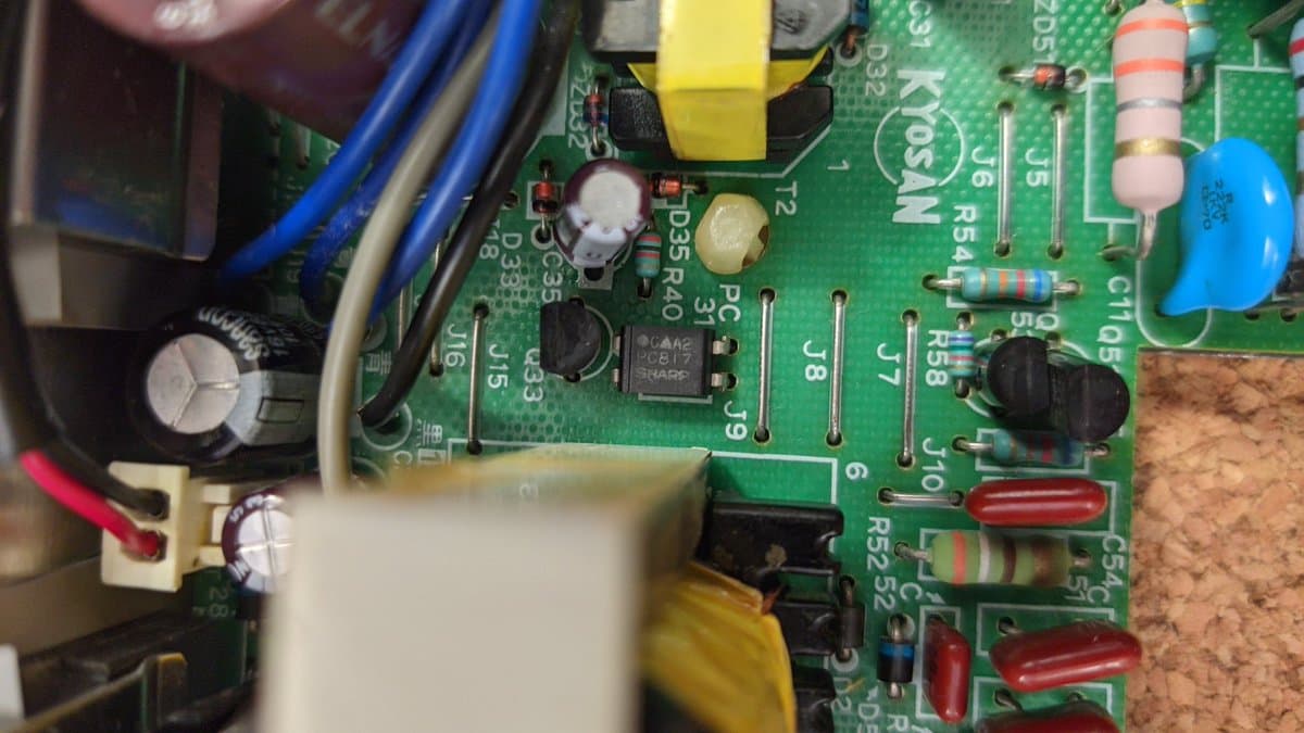 Close-up of Sharp X68000 Pro II PSU board showing components, capacitors, resistors, and a multimeter probe near a photocoupler IC during voltage testing.