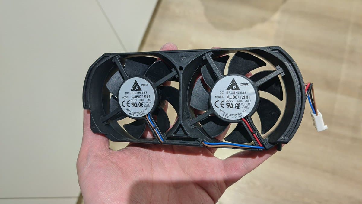Two Delta AUB0712HH brushless cooling fans with blue and red wires held in palm, removed from Xbox 360 during laser replacement repair.