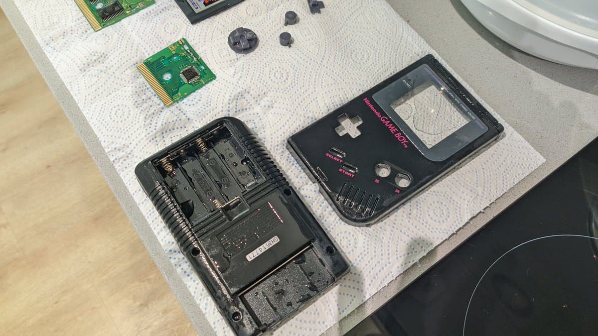 Game Boy Play It Loud disassembly: motherboard, battery contacts, speaker, LCD bracket, and circuit boards on work surface.