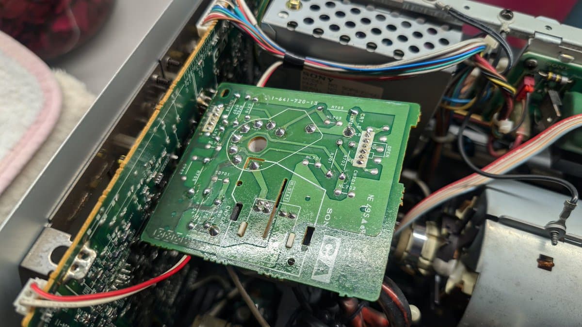 Green PCB with dull solder joints being reflowed during Sony PVM-9045QD PSU restoration. Multicolored wire harnesses visible.