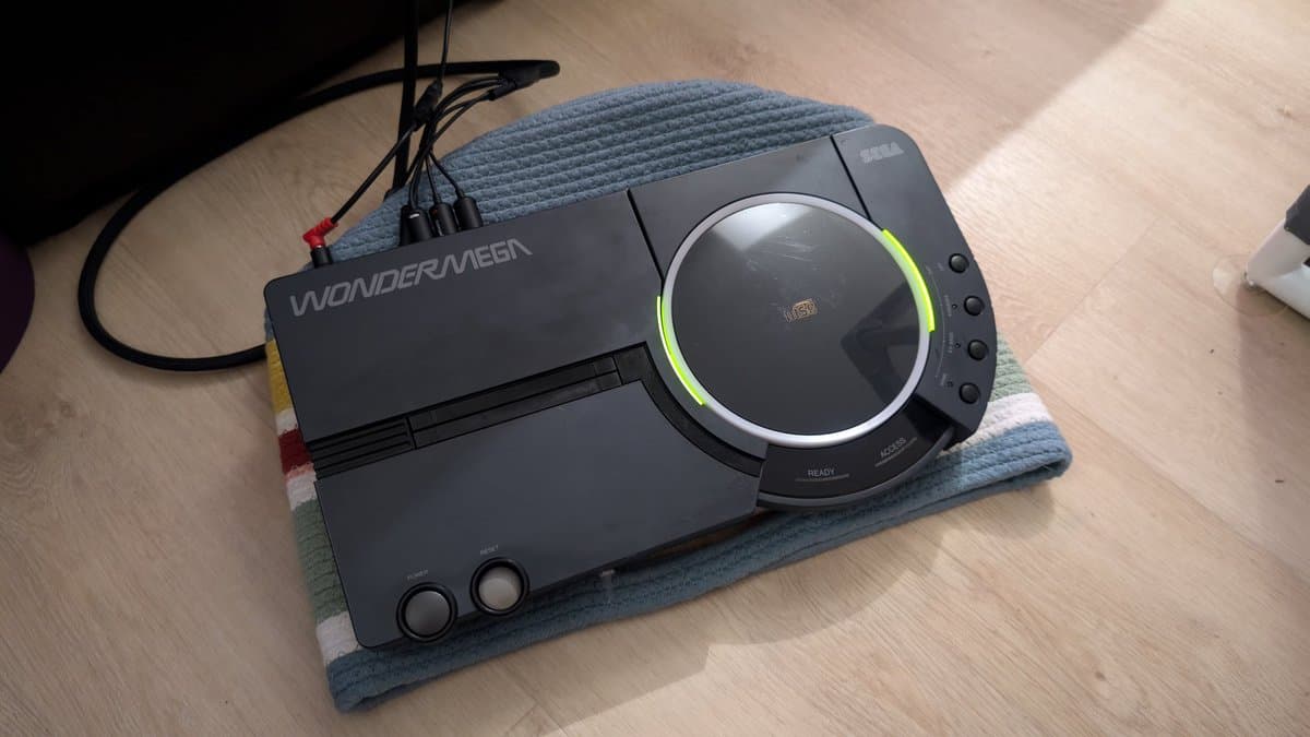 Repaired Sega Wondermega HWM-5010 console on workbench with reassembled halves connected by cable, green LED lit on disc drive.