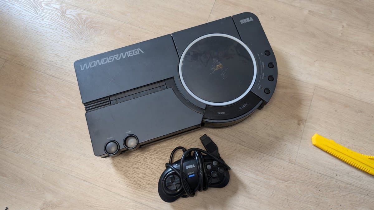 Sega Wondermega console with controller and yellow tool on wooden surface, showing unit awaiting repair.