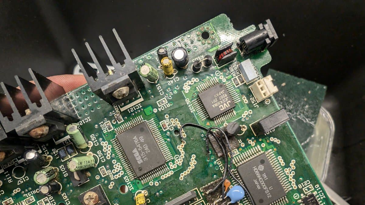 Wondermega board after cleanup showing heatsink, corroded transistor/regulator with fading, multiple ICs, and potential trace damage from corrosion.