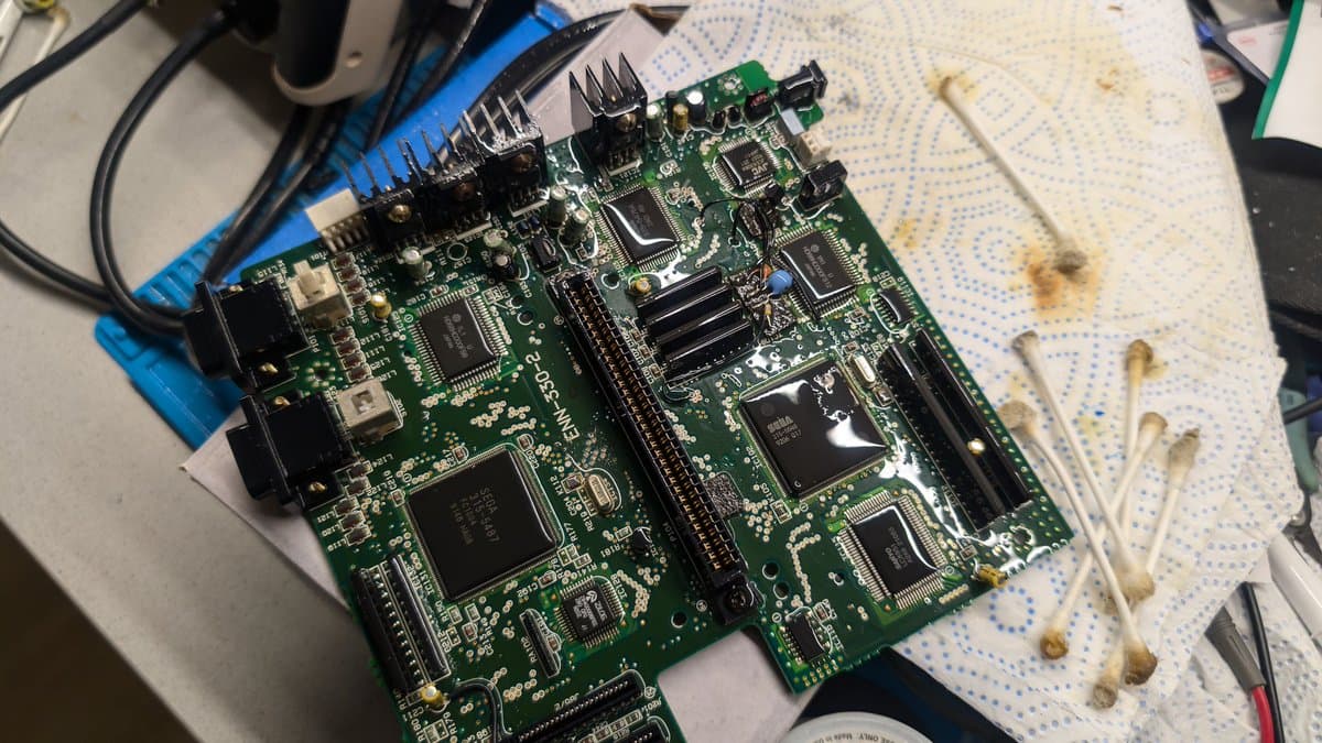 Cleaned Wondermega main board on blue mat with isopropyl residue visible; multiple ICs and connectors exposed after corrosion removal.