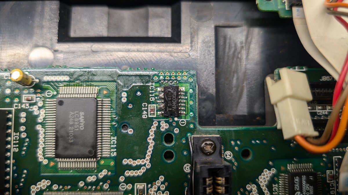 Close-up of Sega Wondermega PCB showing IC116 with suspicious dual-pin solder bridge, corrosion, and adjacent components including RAM package.