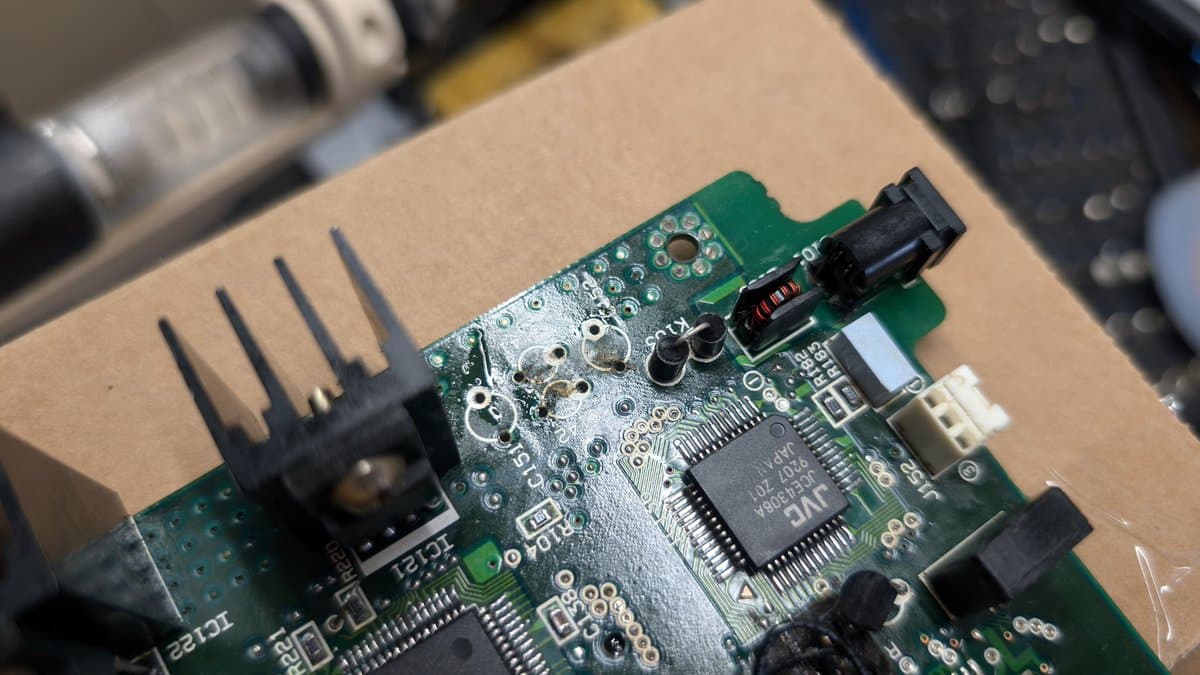 Wondermega mainboard with removed voltage regulator and capacitor, showing exposed solder pads and adjacent IC chips during disassembly.