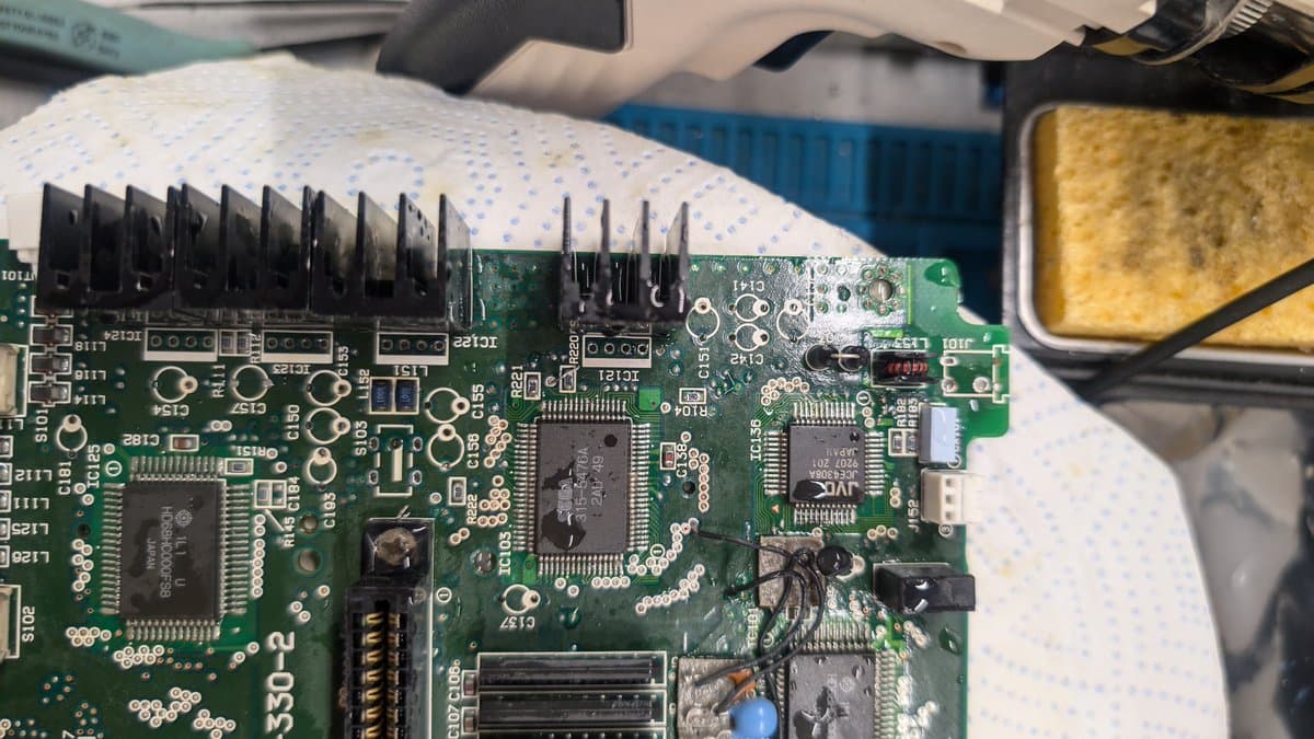 Wondermega PCB half submerged in ultrasonic cleaner after corrosion removal, showing cleaned component area with heatsink fins and solder joints visible.