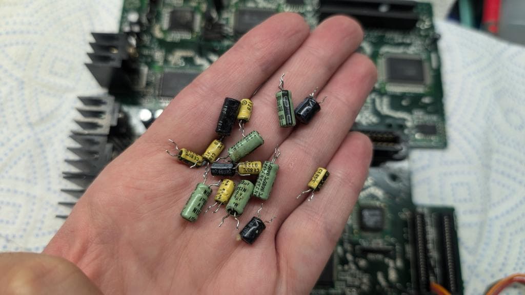 Handful of electrolytic capacitors with yellow and green bodies removed from Wondermega board during repair work.