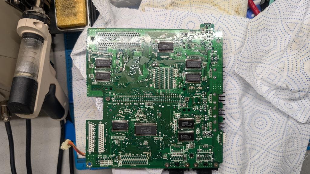 Sega Wondermega main board with soldering iron and desoldering pump positioned for cartridge connector removal to inspect broken trace damage.