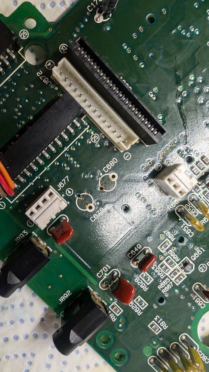 Sega Wondermega circuit board showing corroded components, leaking capacitors (red, marked C70, C840), and connector damage during restoration work.