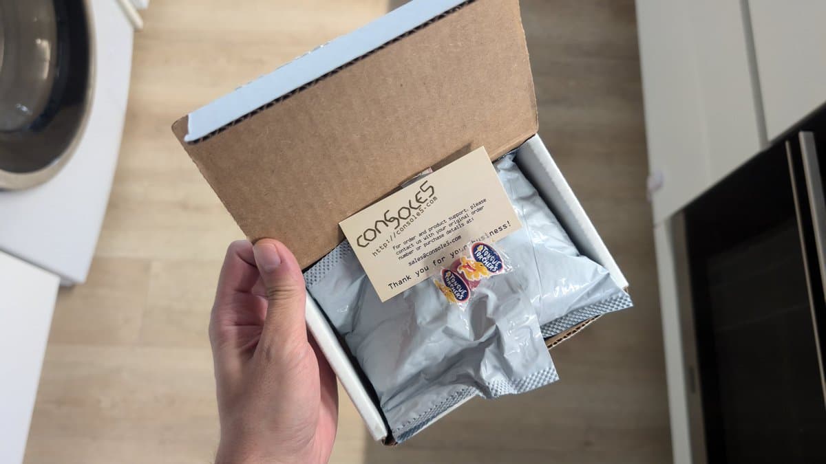 Hand holding open Console5 cardboard box containing silver drive belt package and thank you card for Sega Wondermega repair.