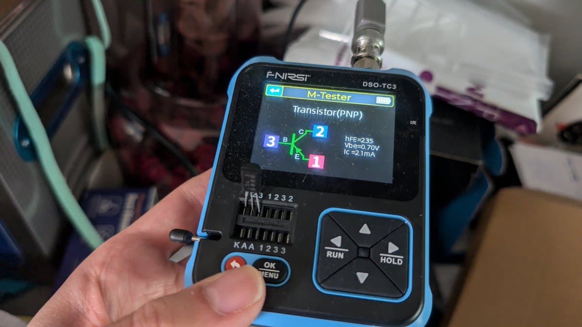 FNIRSI DSO-TC3 multimeter displaying transistor test results (hFE=235, Vbe=0.70V, Ic≥2.1mA) for replacement parts from UTSource during Wondermega repair.
